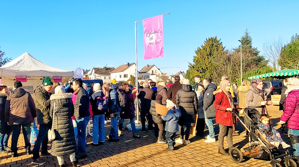 Viele Menschen auf dem Marktplatz, eine Mutter schiebt einen Kinderwagen, im Hintergrund ein Marktstand, über allem weht die Fahne von Egelsbach ist mehr