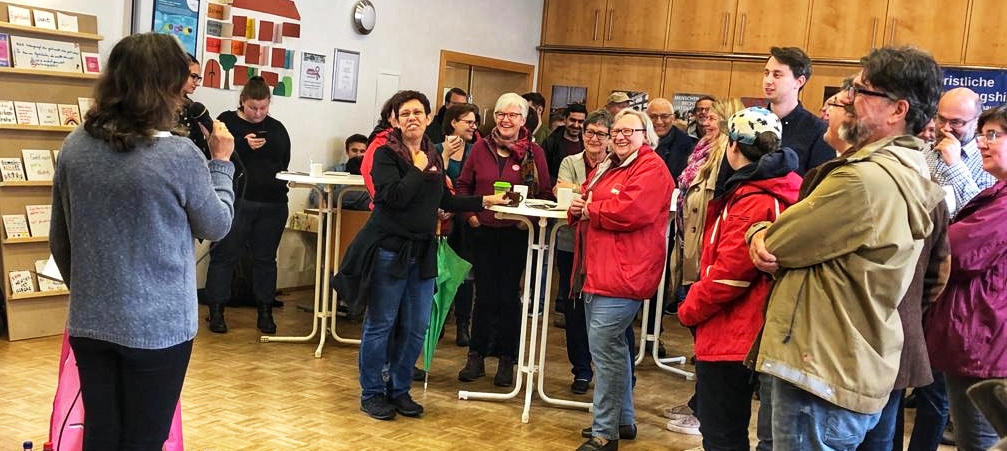 Ein Schaar Menschen im Egelsbacher Gemeindesaal, die einer Sprecherin mit Mikro lächelnd zurören.