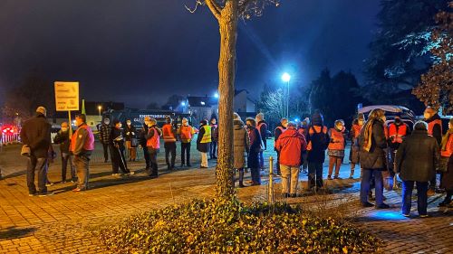 Auf einem beleuchteten Berliner Platz stehen Menschen, teilweise in pinken #EgelsbachIstMehr-Laibchen. Ein Mann hält ein Schild mit Aufschrift, die leider nicht lesbar ist.